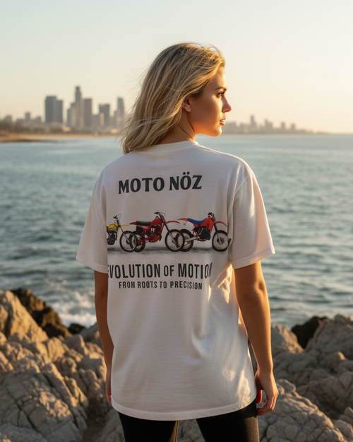 Person wearing a 'Moto Nóz' t-shirt by the water with a city skyline in the background